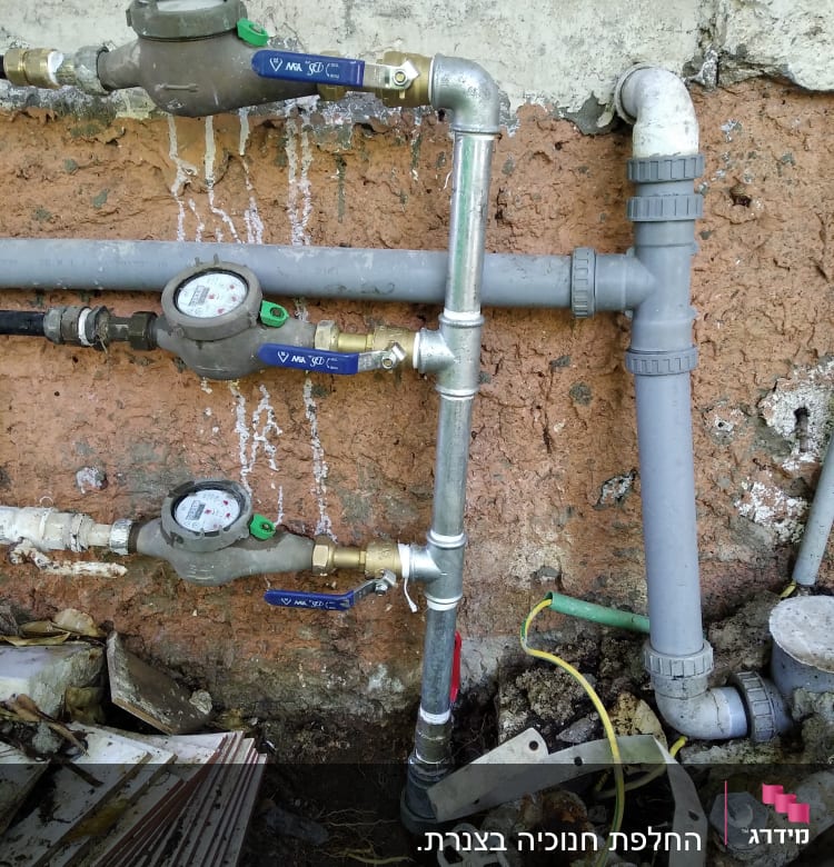 צינורות מים עם מד מים וברזים על קיר